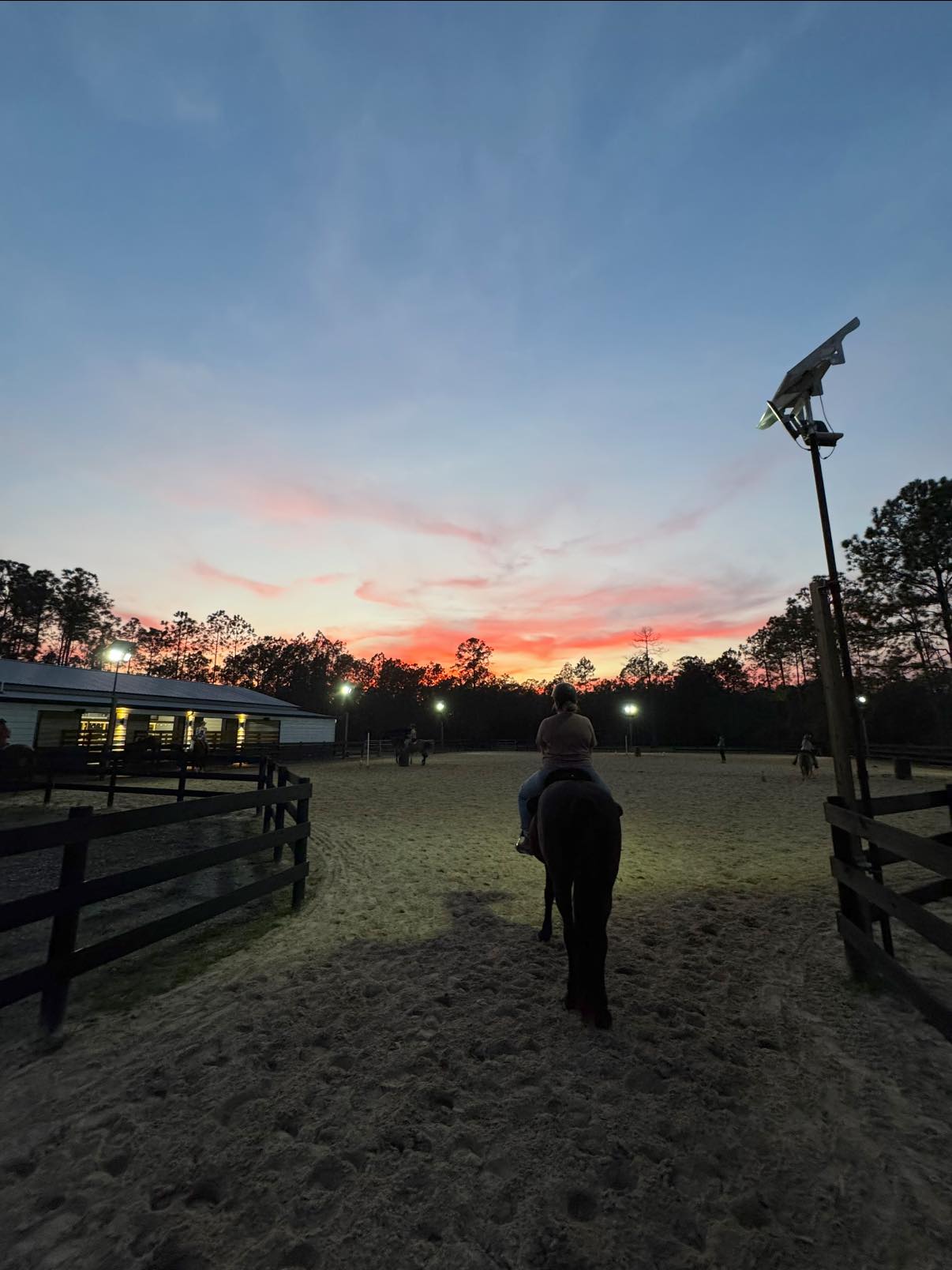 Horse and rider entering lighted arena at Rodeo Stables during sunset