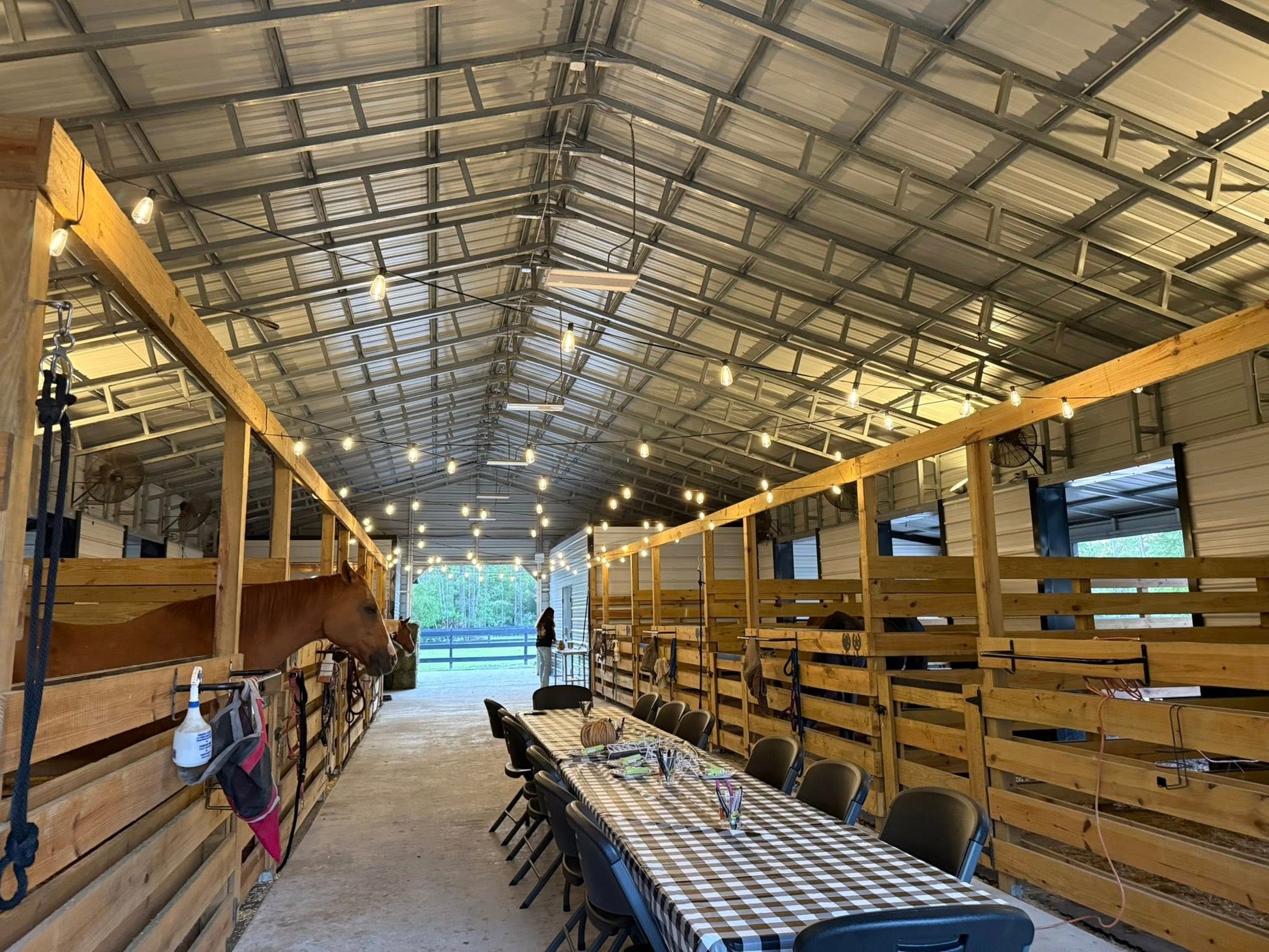 Inside the Rodeo Stables barn event space with horse stalls, string lights, and dining tables in Ormond Beach, Florida.