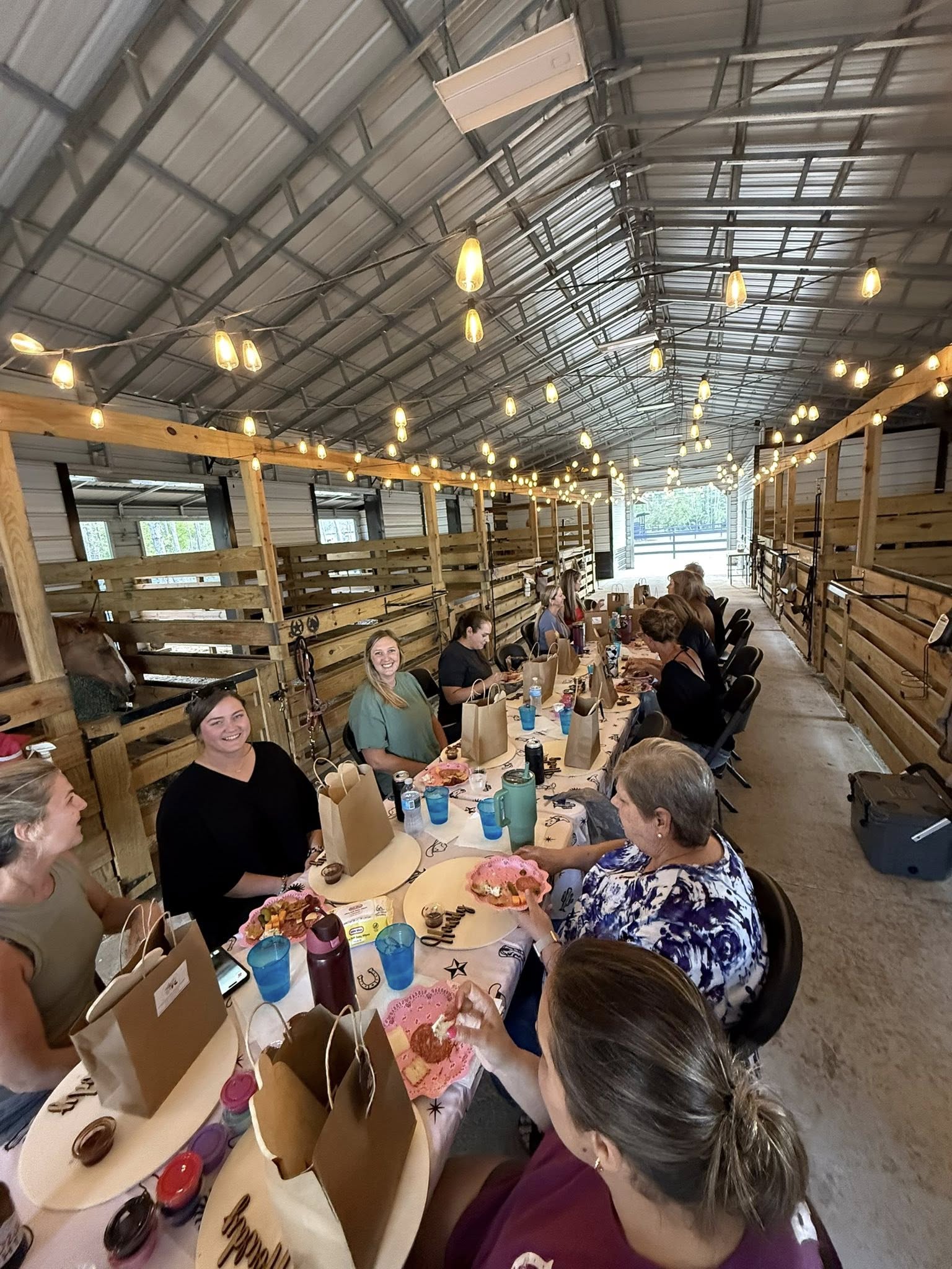 Guests gathered inside the Rodeo Stables barn for a western-inspired dinner event under string lights