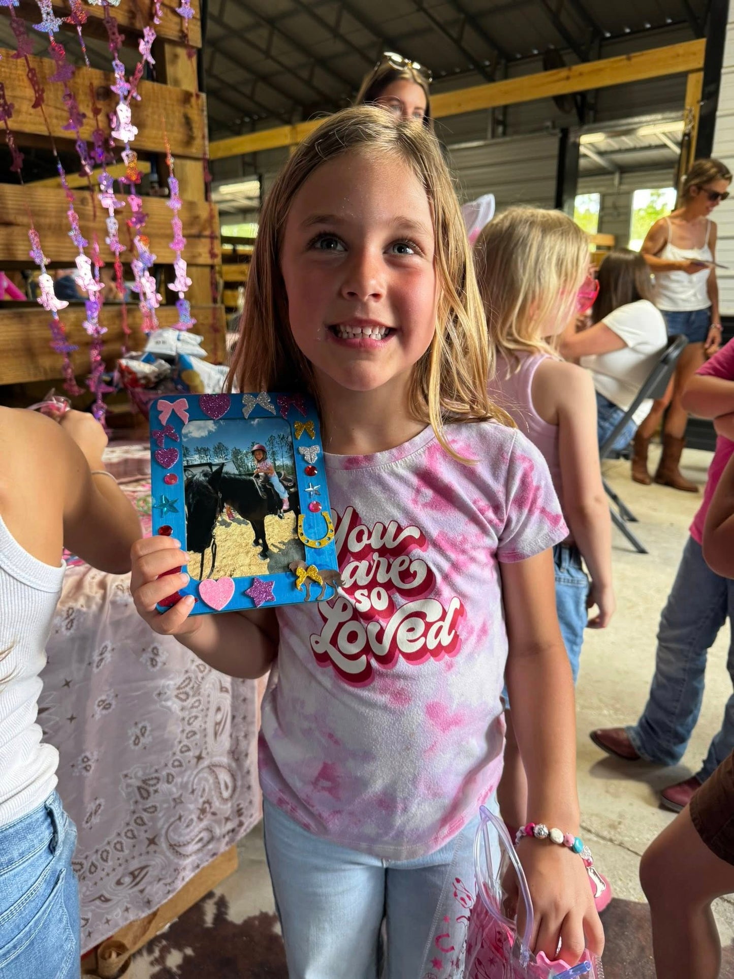 Young girl showing a decorated horse-themed craft during a kids activity at Rodeo Stables.
